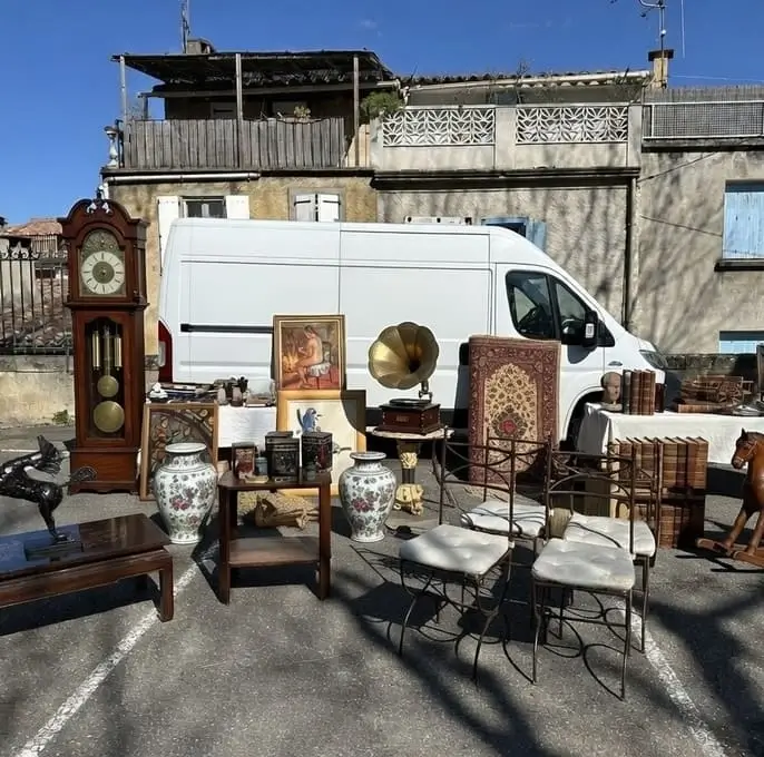 Belle sélection d’objets chinés en brocante avec horloge comtoise, gramophone à cornet doré, vases en porcelaine et chaises vintage, exposés devant le camion utilitaire Seb Troc