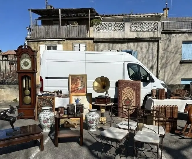 Belle sélection d’objets chinés en brocante avec horloge comtoise, gramophone à cornet doré, vases en porcelaine et chaises vintage, exposés devant le camion utilitaire Seb Troc